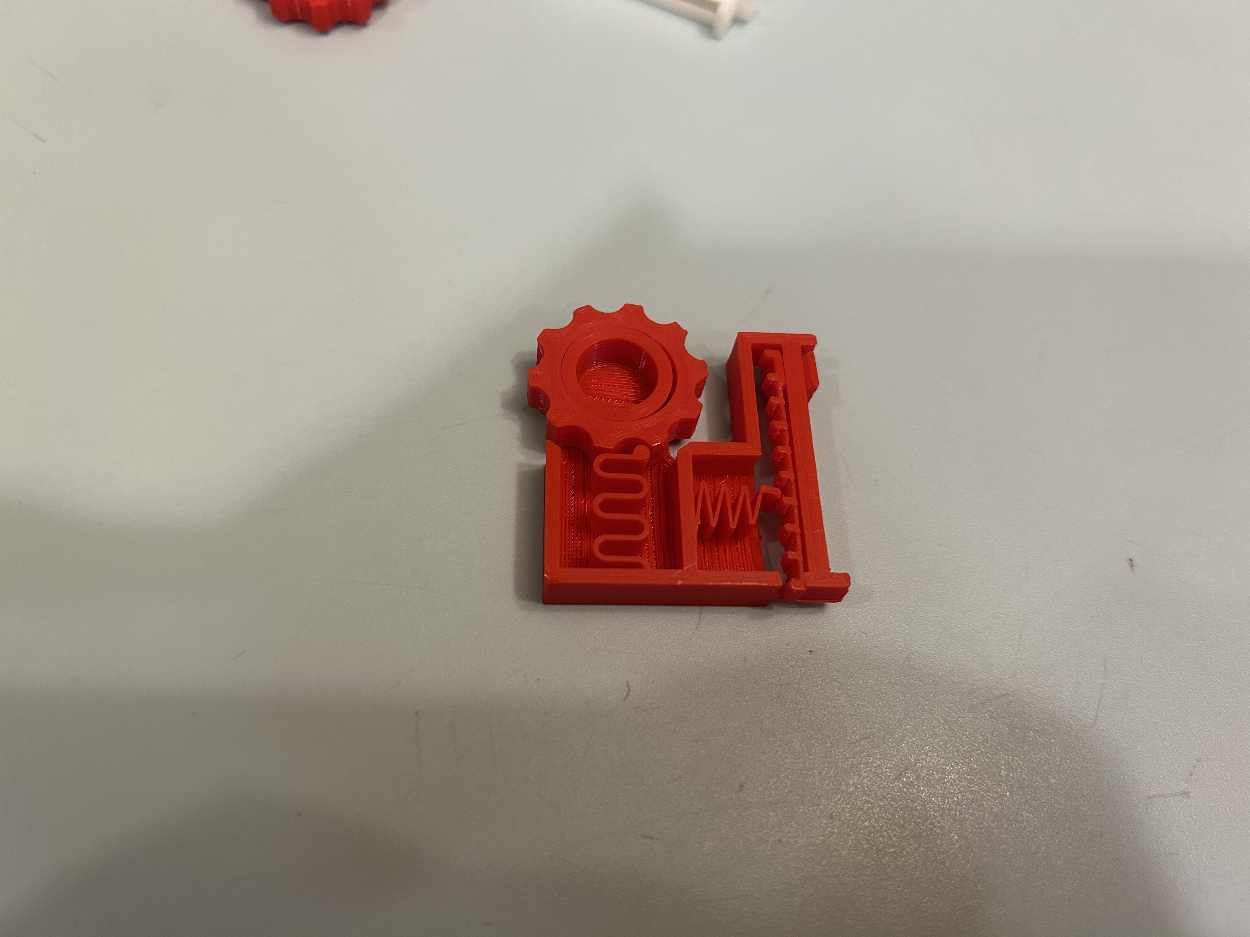 Top view of the final red fidget toy, showing the gear, slider, and springs